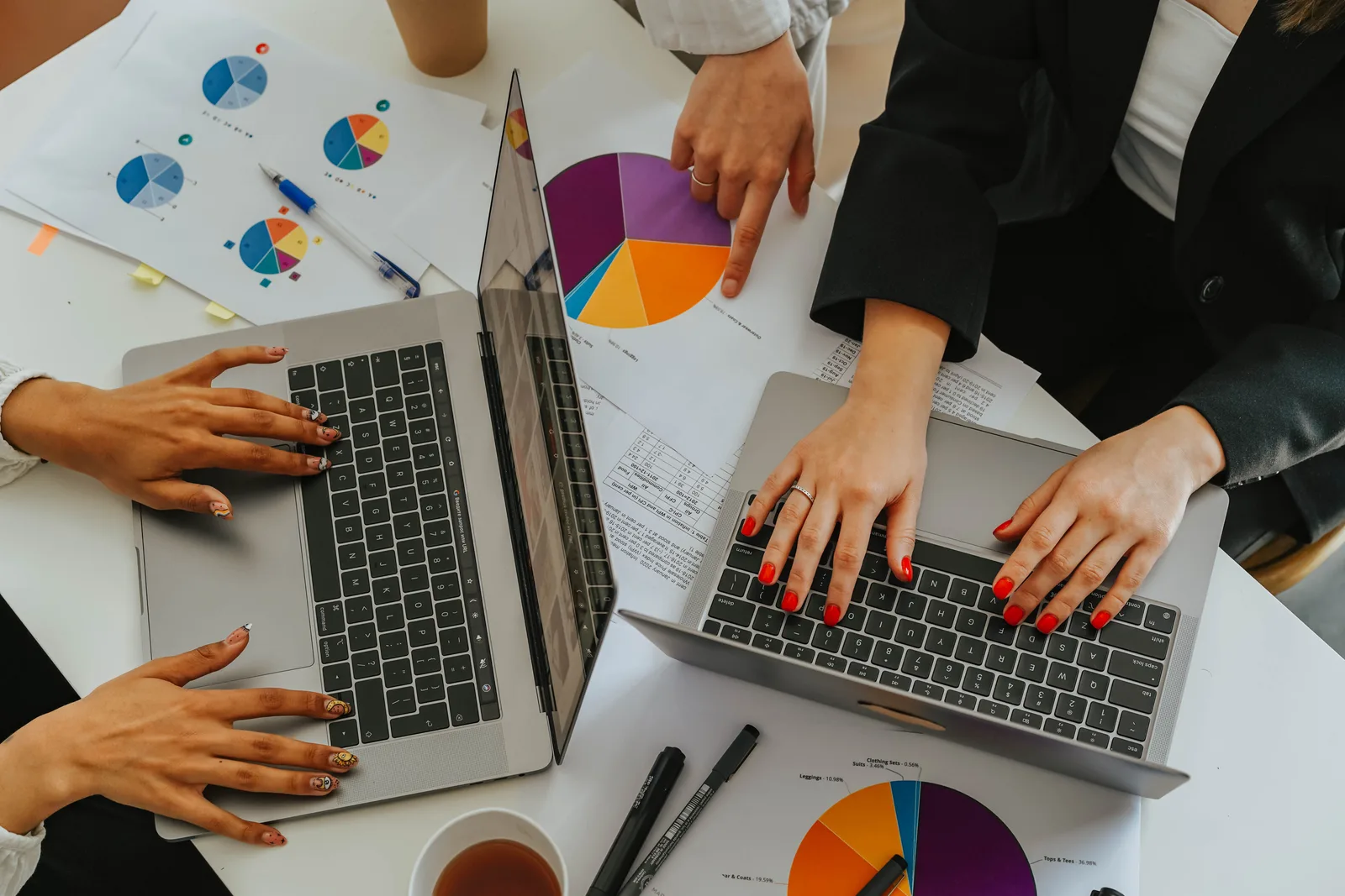Top view of women working together on laptops with business charts at a white office table. Nine YouTube channel revenue metrics to track each month