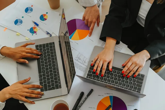 Top view of women working together on laptops with business charts at a white office table. Nine YouTube channel revenue metrics to track each month