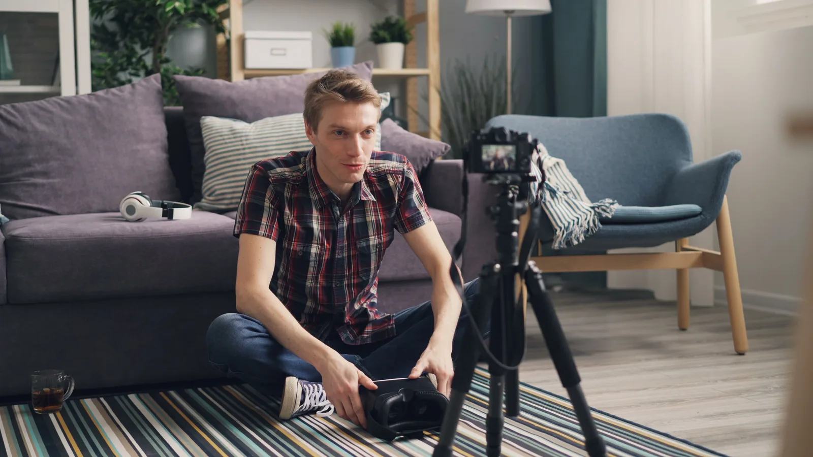 Young man sitting on the floor filming a vlog in a cozy living room with camera and tripod. YouTube Sponsorship Disclosure Rules Canada: Ad Standards vs CRTC